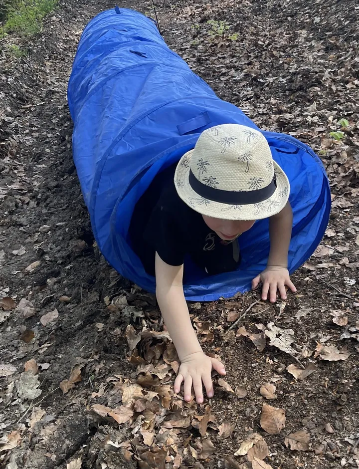 Kind krabbelt bei einer Schnitzeljagd-Station durch einen Spieltunnel im Wald